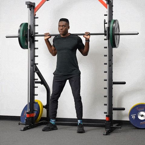 En man utför knäböj i en modern smithmaskin.