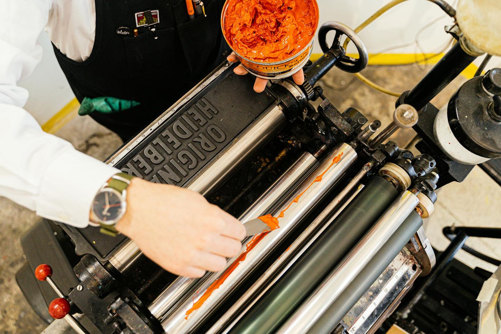 En hantverkare applicerar orange tryckfärg på en Original Heidelberg-tryckpress.
